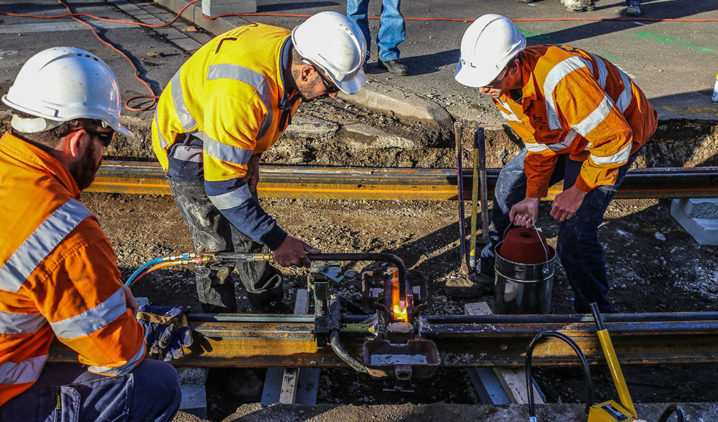 Three men repairing exposed tram track