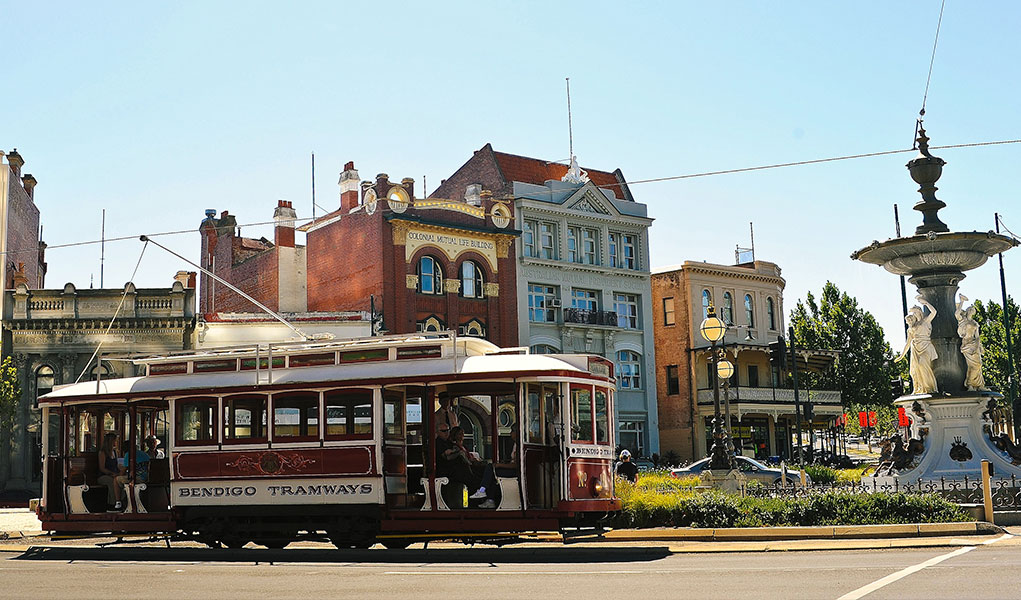 Tram full of passengers passing historic buildings in Bendigo